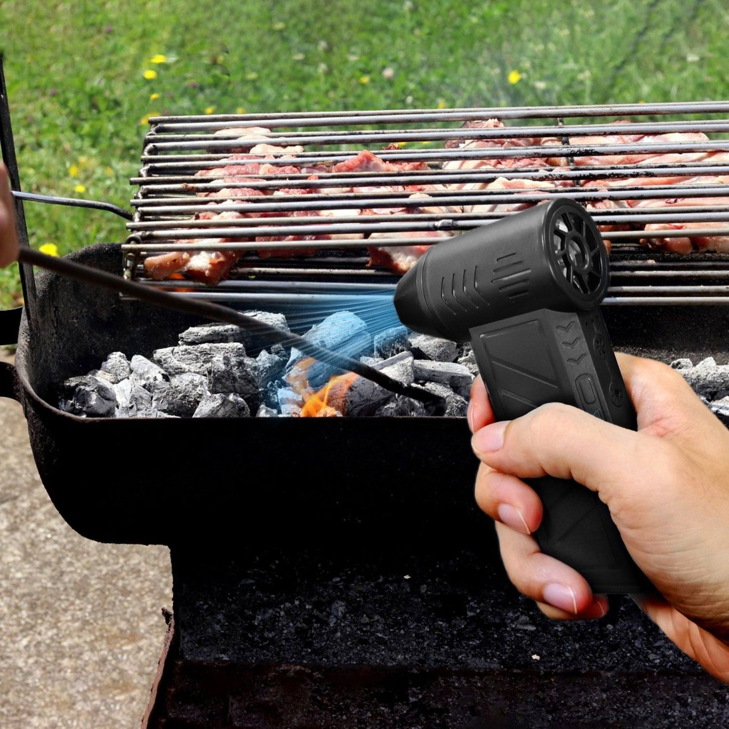 Person using a handheld air duster for grilling to light charcoal on a barbecue grill outdoors