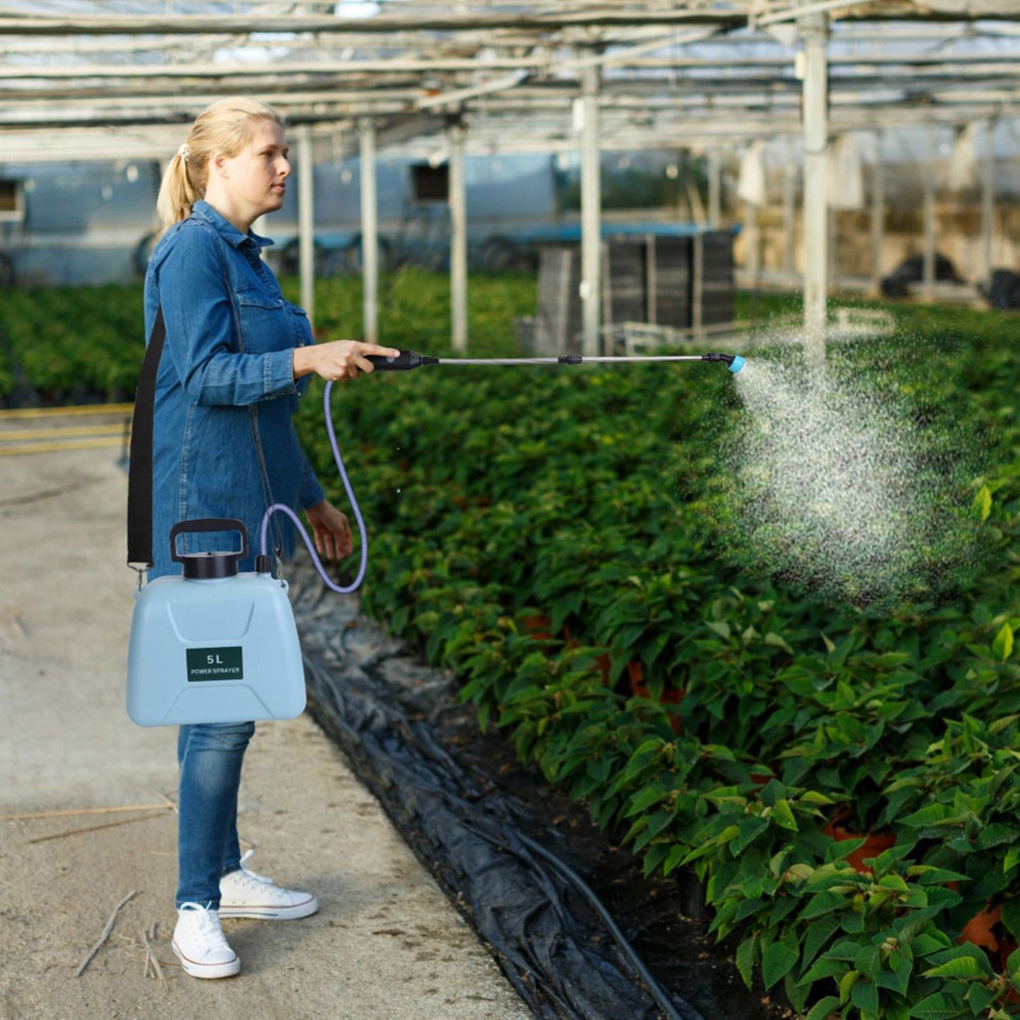 Person using an electric plant sprayer to spray plants in a greenhouse