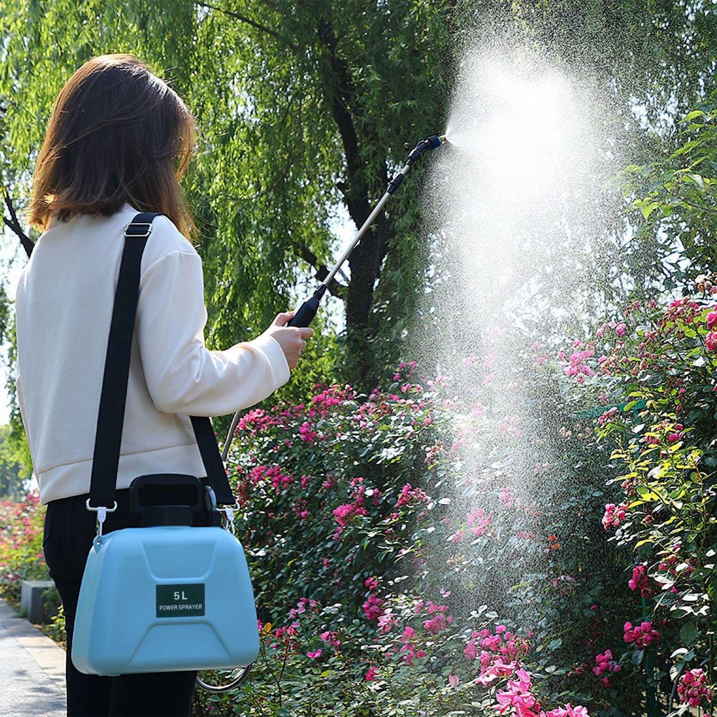 Person using an electric plant sprayer to water plants in a garden